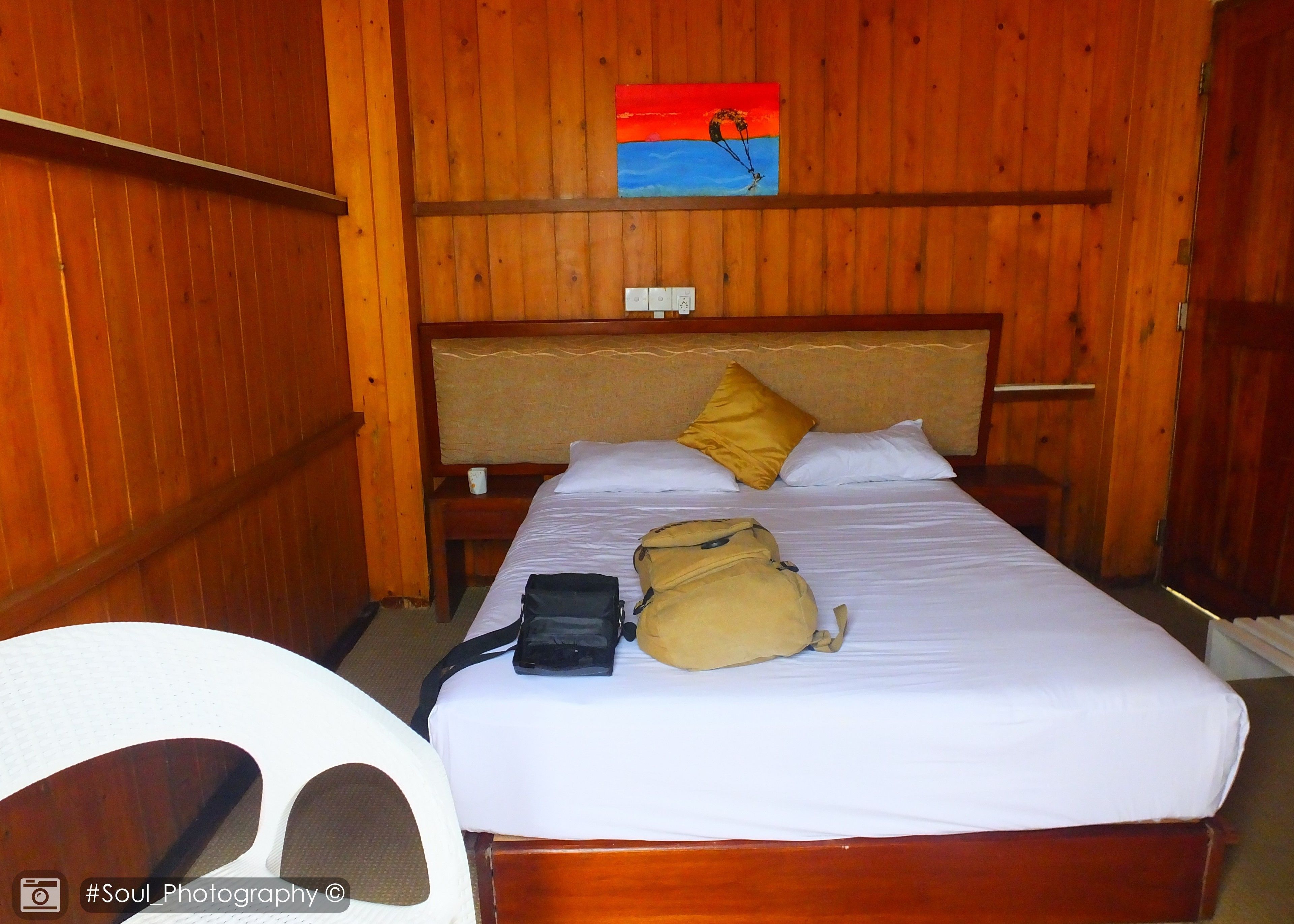 Ein Zimmer mit Holzvertäfelung, einem Bett, einem Nachttisch, einem Sessel und einem Bild an der Wand.