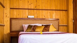 Een kamer met houten lambrisering, een bed, een nachtkastje en een stopcontact aan de muur.