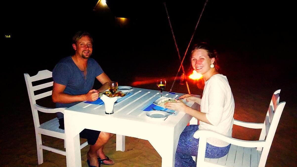 Dos personas sentadas en una mesa blanca con una copa de vino, un plato de comida y una botella de agua.