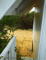Uma trilha de areia leva a uma área coberta com grades brancas e vegetação.