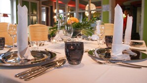 A dining table set with silverware, plates, and glasses, with a vase of flowers in the center.