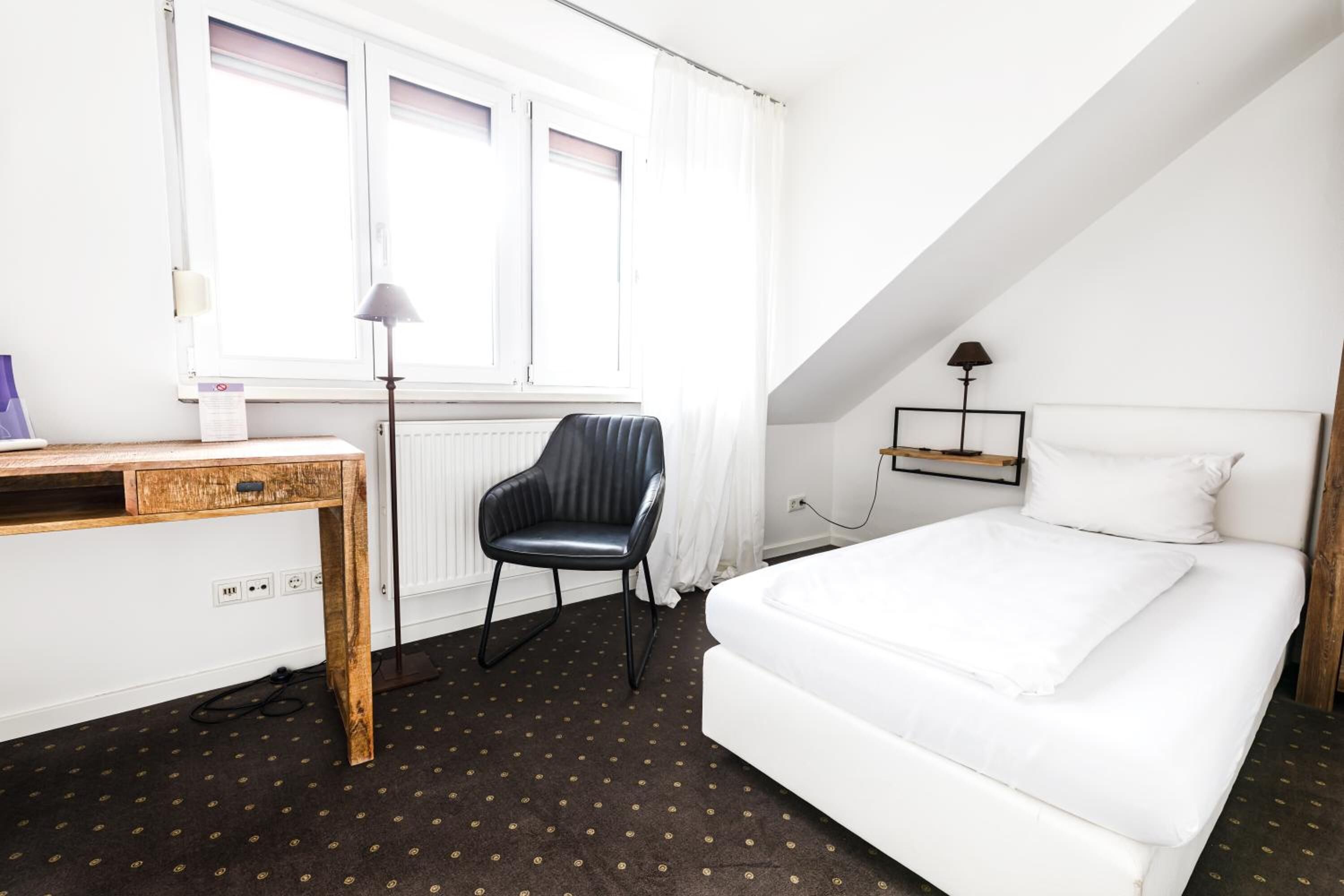 A bedroom with a bed, a desk, a chair, and a window with curtains.