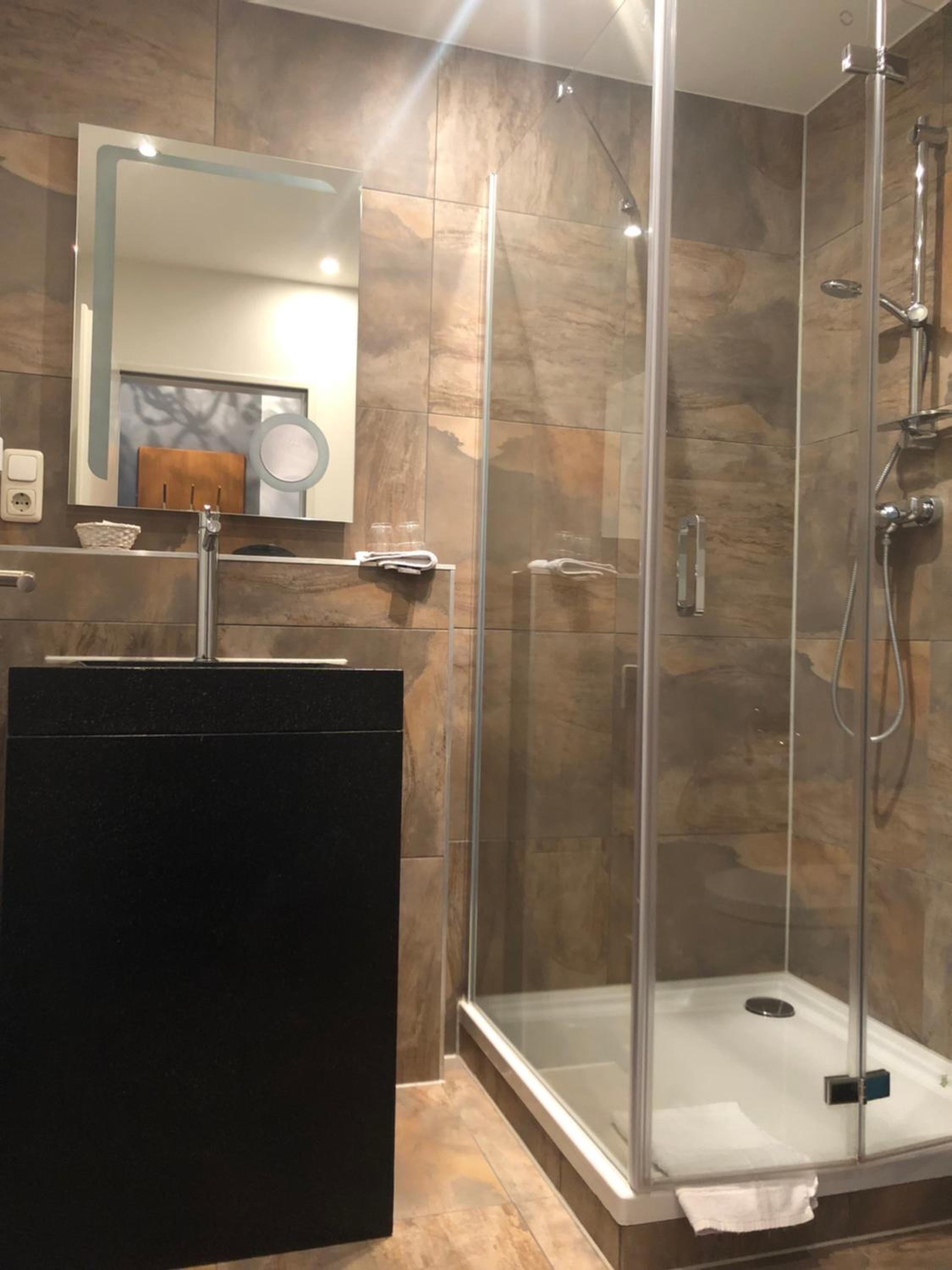 Un baño moderno con ducha de vidrio, un lavamanos negro y un espejo encima.