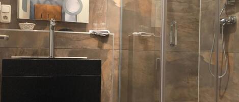 Un baño moderno con ducha de vidrio, un lavamanos negro y un espejo encima.