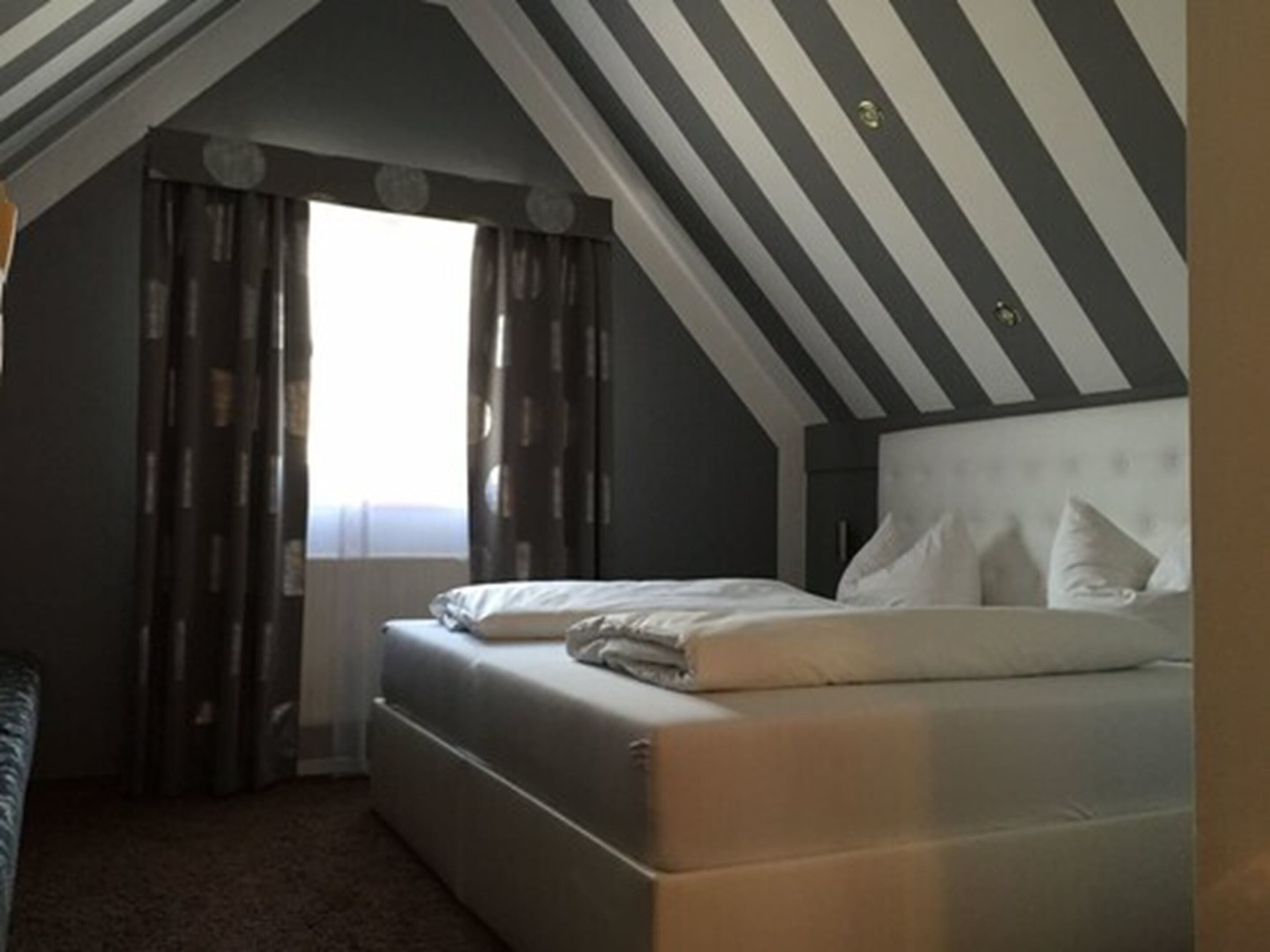 Un dormitorio con cama, ventana con cortinas y techo inclinado.