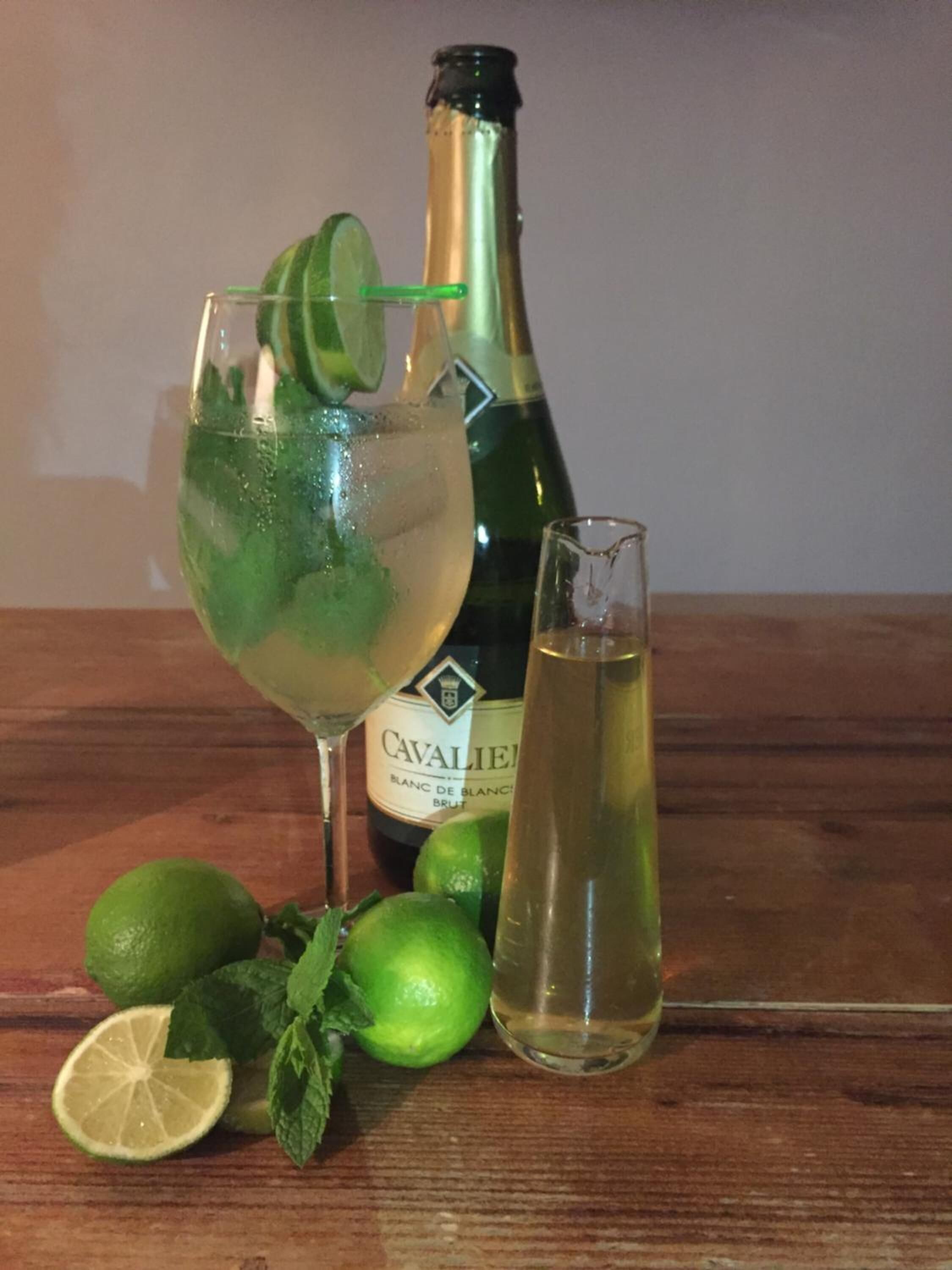 Una ampolla de cava CAVALIER, un got amb una taronja i un altre got de cava sobre una taula de fusta.