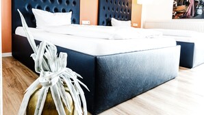 A modern hotel room with a large bed, a dark headboard, and a wooden floor.