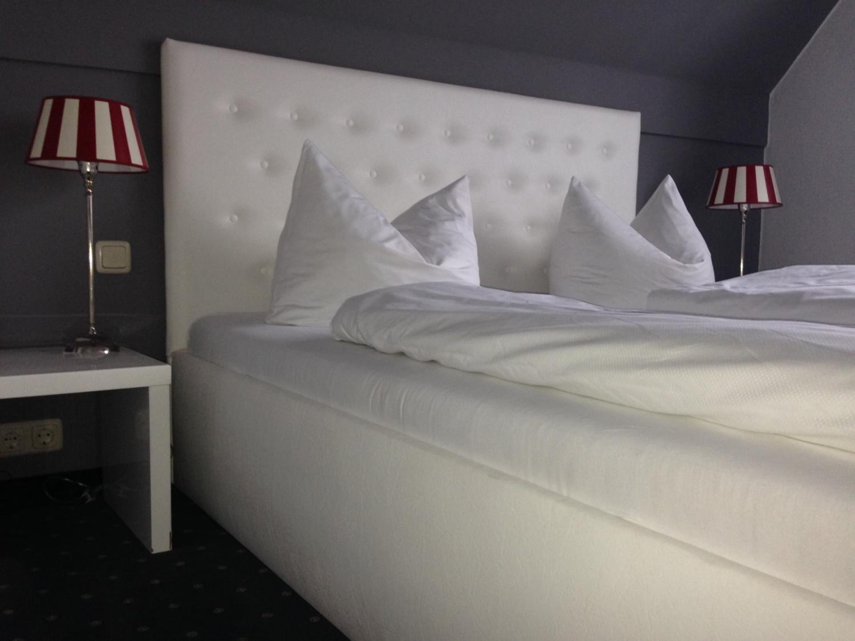A hotel room with a large bed, white bedding, and two bedside lamps with red and white stripes.
