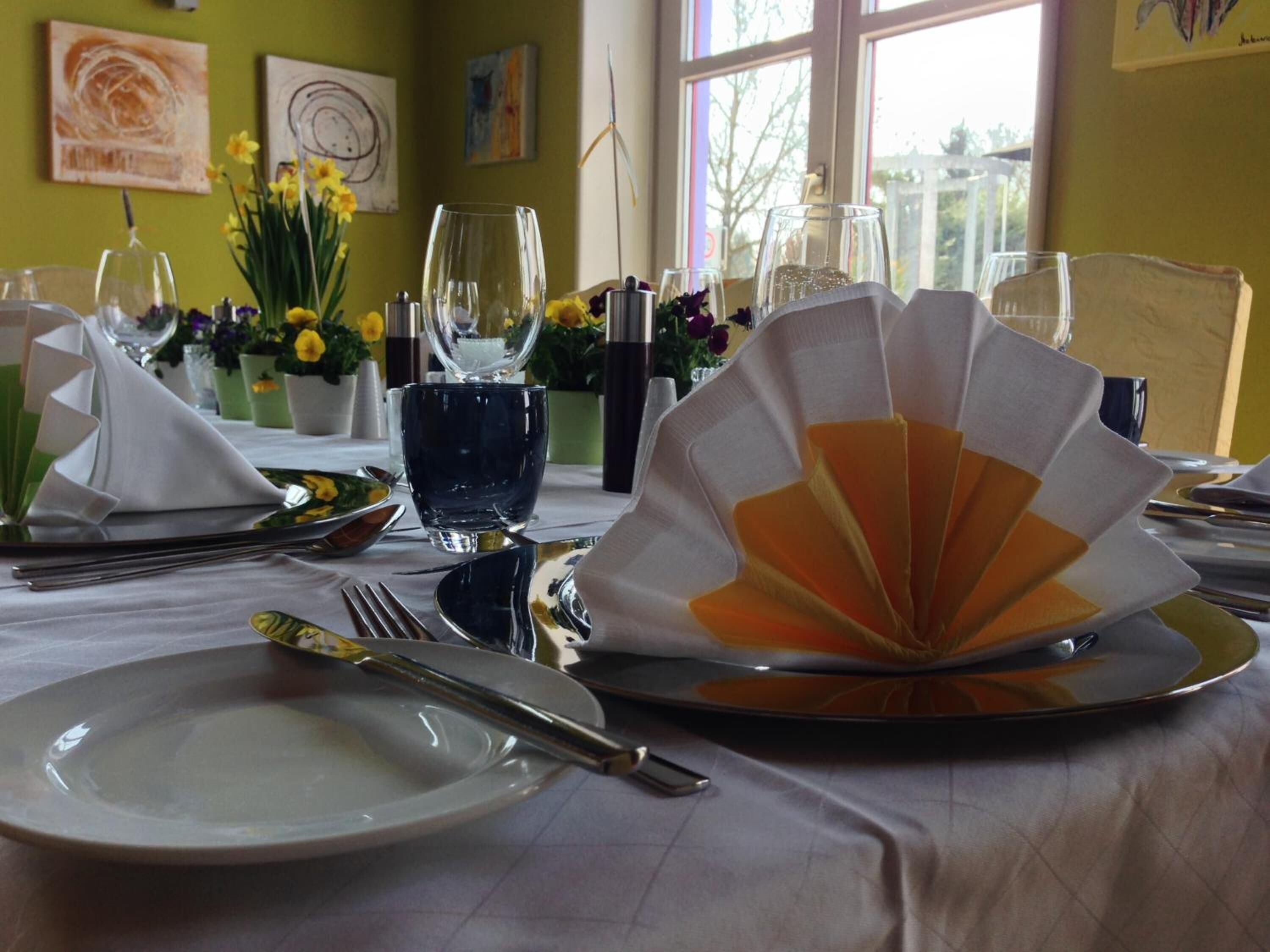 Une table à manger dressée avec des assiettes, des couverts et un centre de table en forme d’éventail.