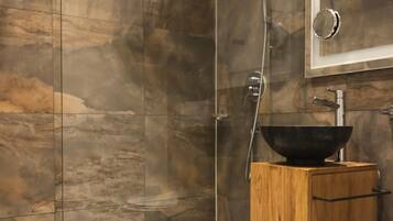 A modern bathroom with a glass-enclosed shower, a wooden vanity with a black basin, and a large mirror.