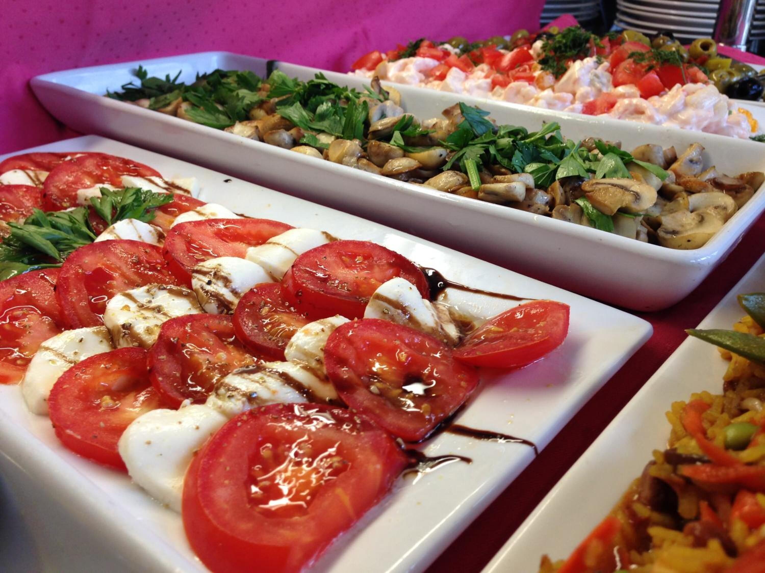 Ein Buffet mit verschiedenen Gerichten, darunter ein Tomate-Mozzarella-Salat, ein Seafood-Salat und ein Reisgericht mit Gemüse.
