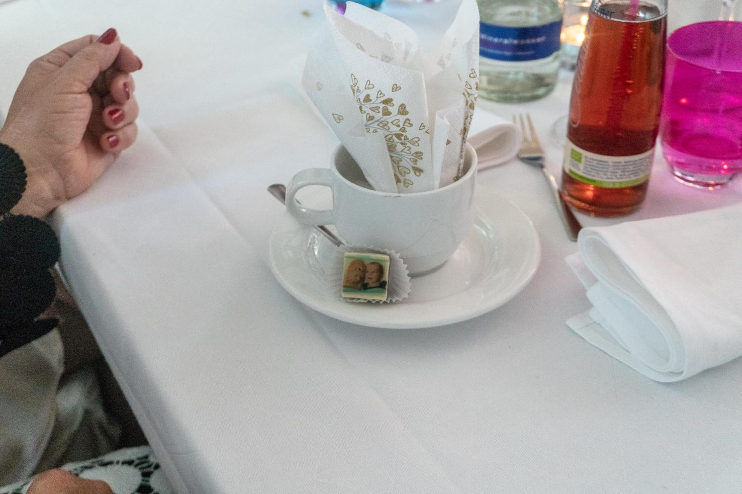 A table with a white cup containing a tea bag, a glass of pink liquid, and a bottle of amber liquid.
