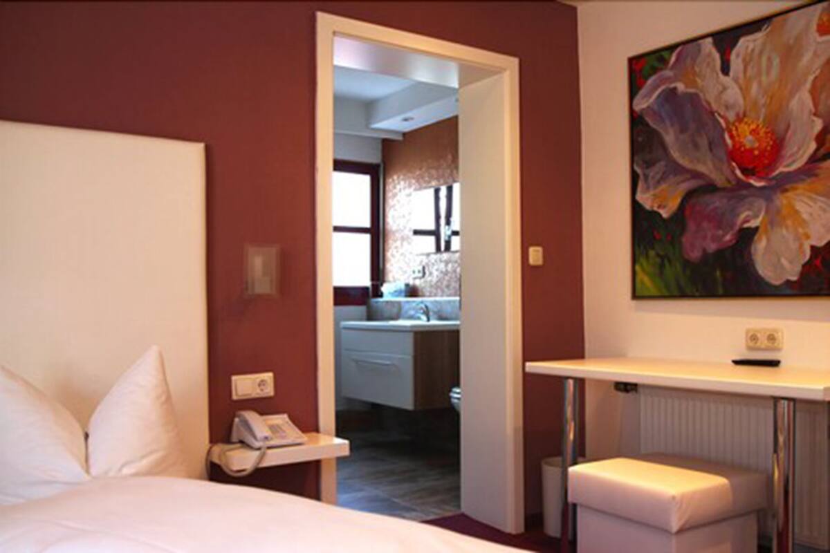 Een hotelkamer met een bed, een bedtafel, een telefoon en een bloemen schilderij aan de muur.