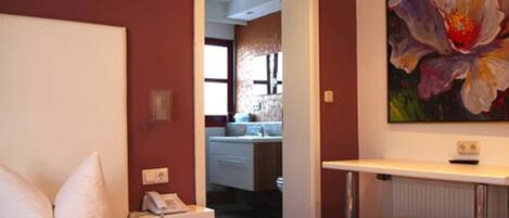 A hotel room with a bed, a bedside telephone, a small table, and a painting of a flower on the wall.