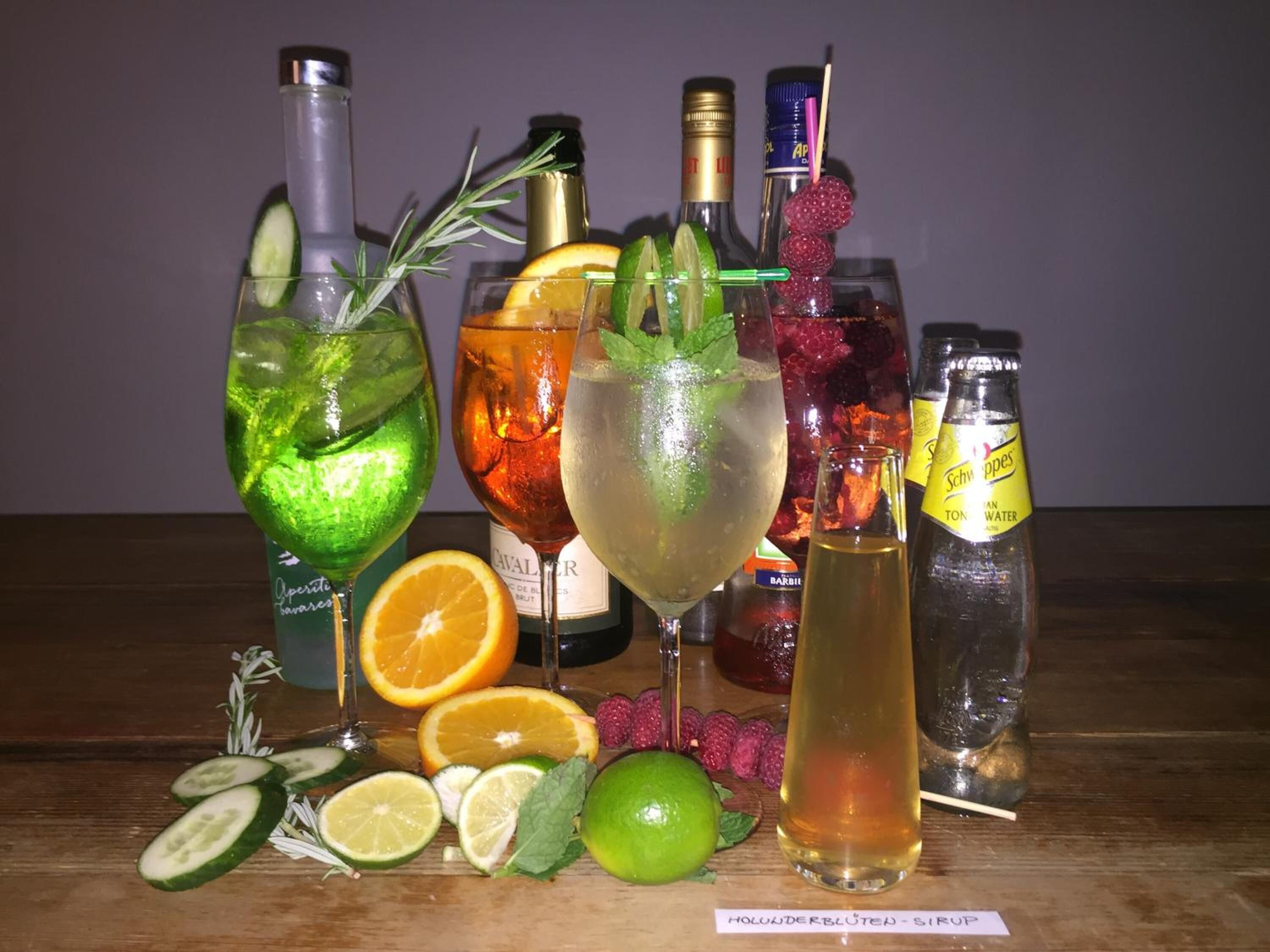 A variety of drinks with garnishes and bottles of water and alcohol on a wooden table.