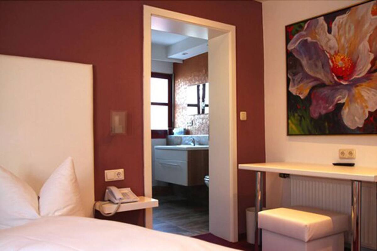 Een hotelkamer met een bed, een telefoon op het nachtkastje, een klein tafeltje, een radiator en een schilderij aan de muur.