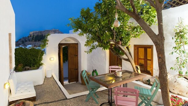 A cozy outdoor seating area with a table and chairs, surrounded by white walls and a tree.