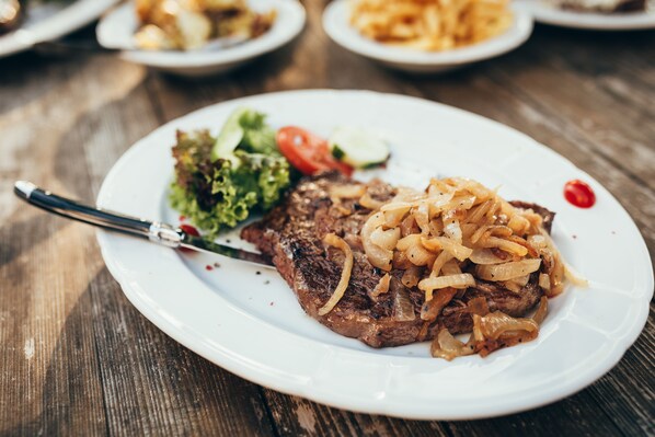 Un plato con bistec, cebollas y una ensalada como guarnición sobre una mesa de madera.