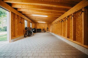 Zona cubierta para guardar bicicletas con paredes de madera, suelo de baldosas y bicicletas estacionadas adentro.