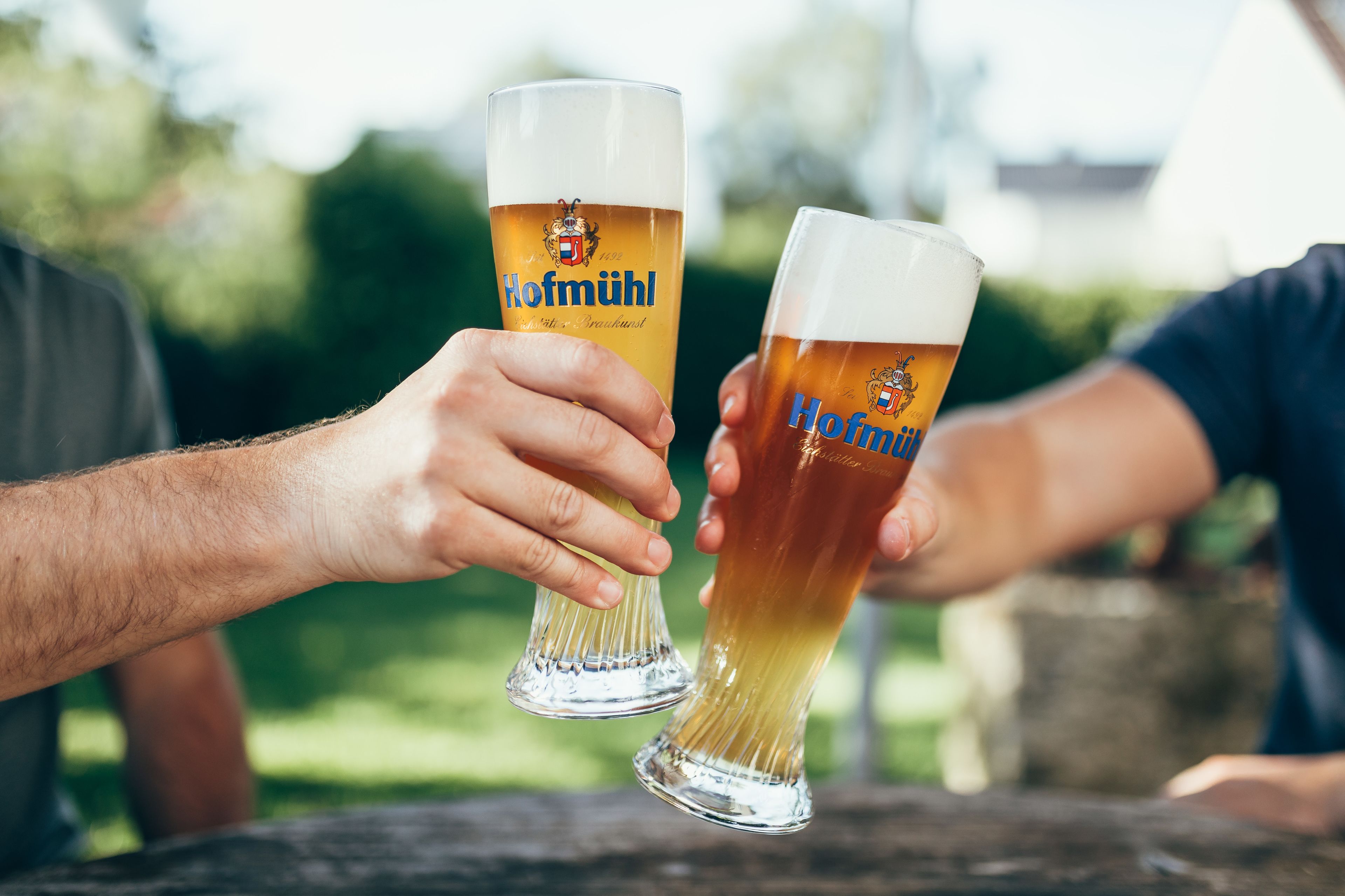 Dos personas sosteniendo vasos de cerveza Hofmüll.