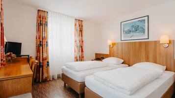 A hotel room with two beds, a wooden desk, a TV, and a framed picture on the wall.
