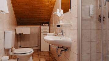 A bathroom with a wooden ceiling, a shower, a toilet, and a sink.