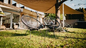 Two outdoor chairs under a shade sail, a grassy area, and a building with a balcony. - Hirschenwirt (Eichstaett)