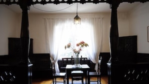 A dining area with a table and chairs, a hanging light fixture, and a window with curtains. - Casagrande-Grosshaus (Laives)