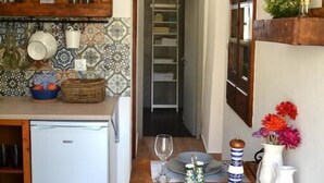 A compact kitchen with a refrigerator, wooden shelves, and a patterned backsplash. - CasaLindos Spitaki (Rhodes)