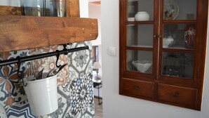 A kitchen with a wooden shelf holding glassware, a white bucket with utensils, and a patterned backsplash. A wooden cabinet with glass doors is visible in the background. - CasaLindos Spitaki (Rhodes)