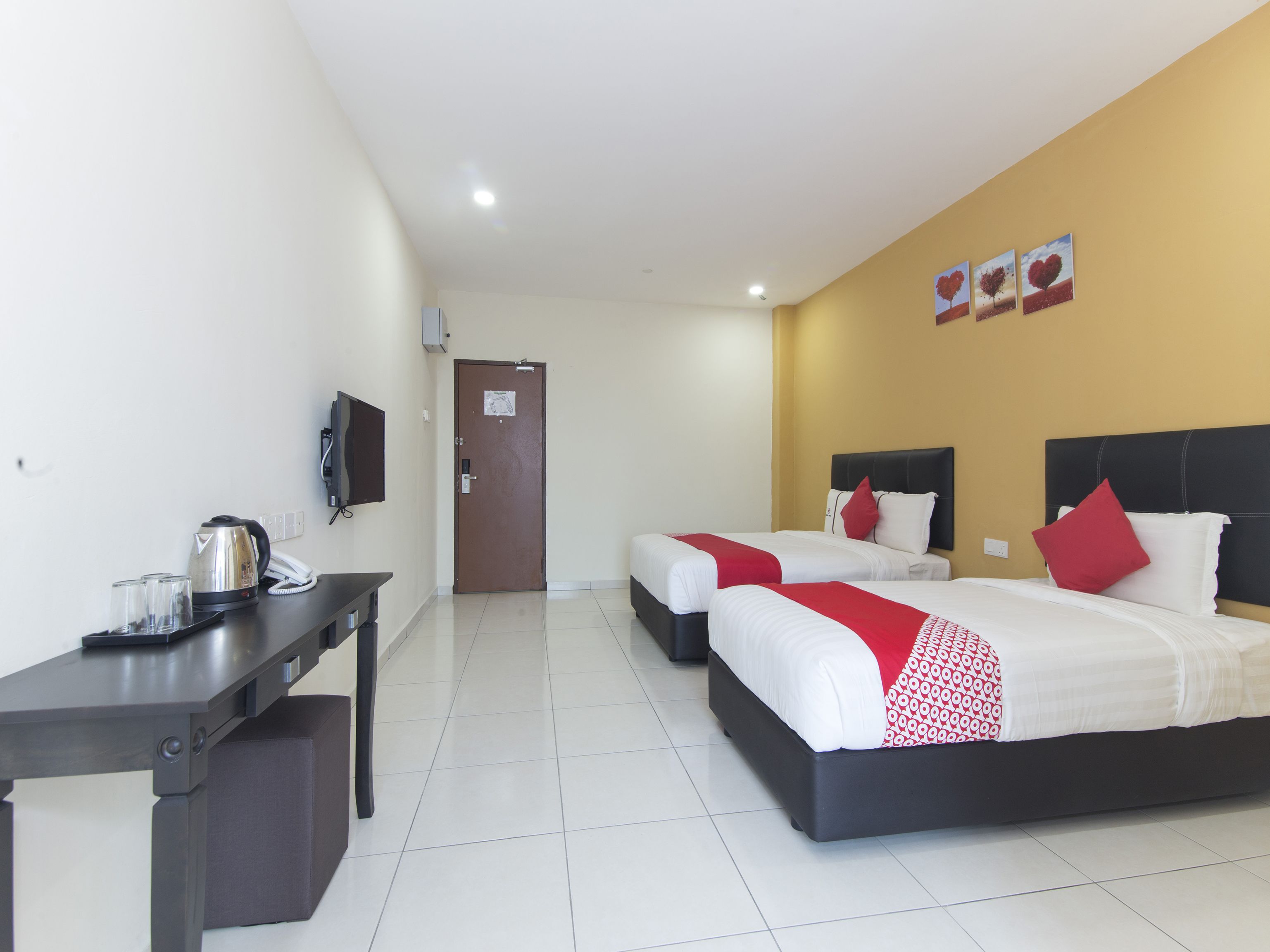 A hotel room with two beds, a desk with a kettle, and a television.