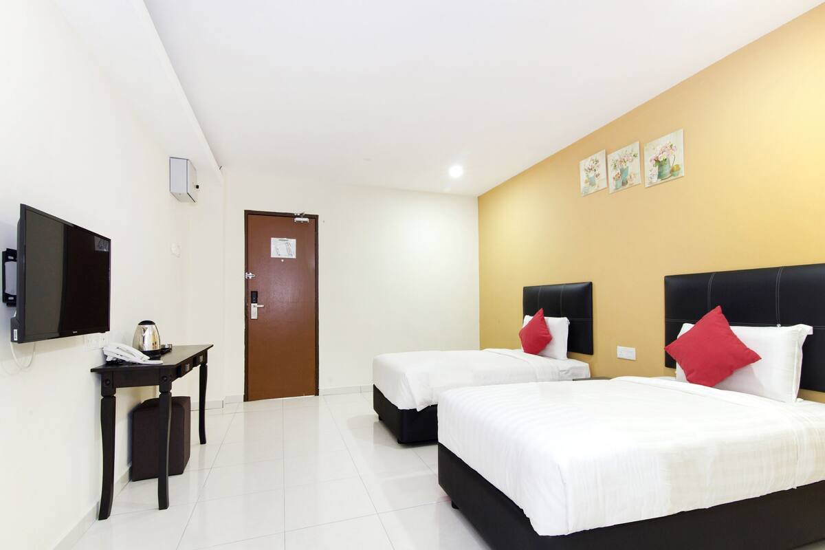 Una habitación de hotel con dos camas, un televisor, una mesa con una tetera y una puerta.