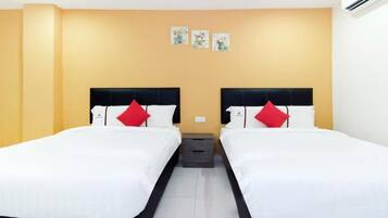 A hotel room with two beds, each with a black headboard and white bedding, and red pillows. There are three small wall art pieces above the beds.
