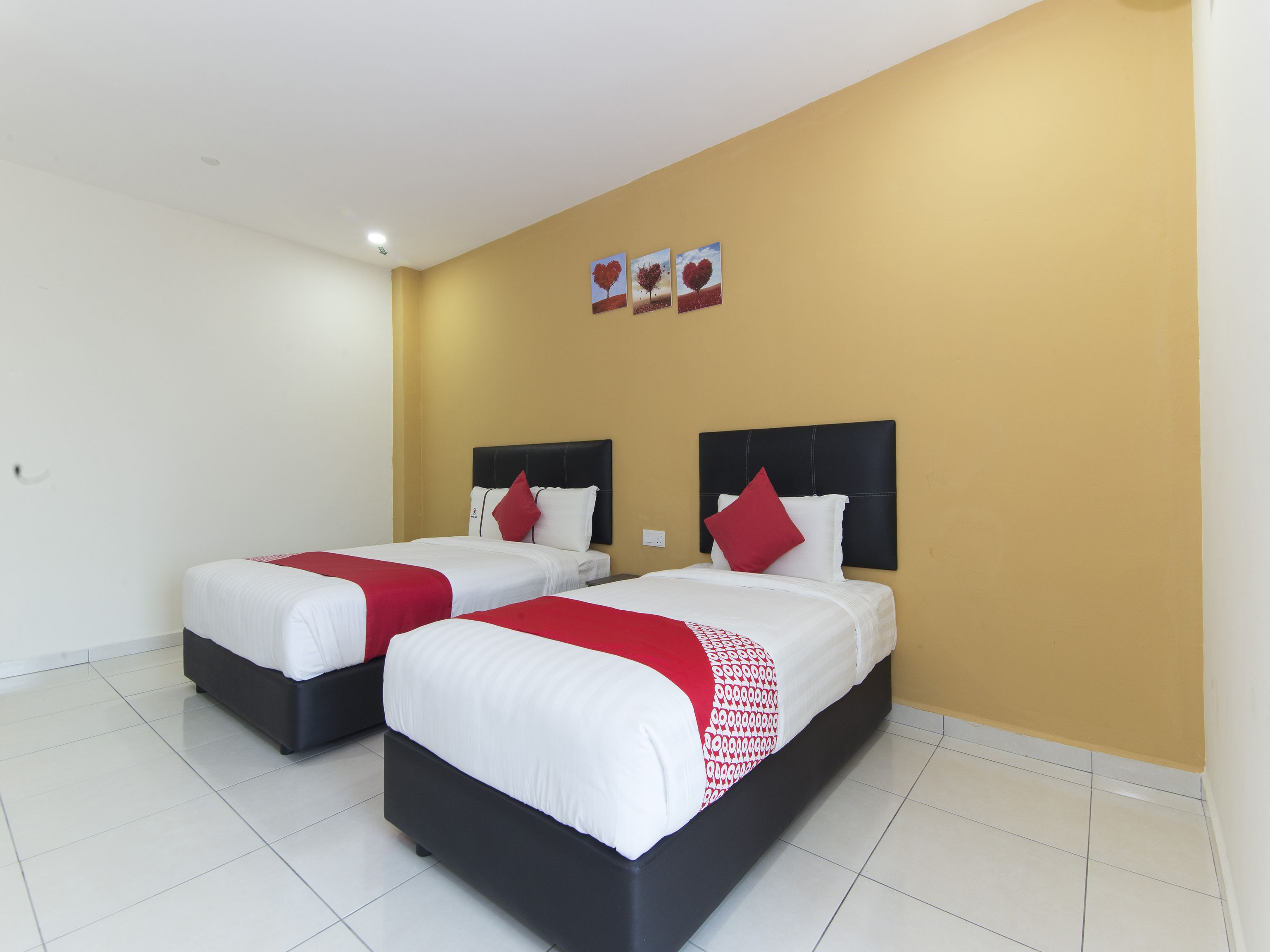 A hotel room with two beds, white bedding, red accents, and a yellow accent wall.