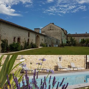 A stone building with a large lawn and a swimming pool with lounge chairs.