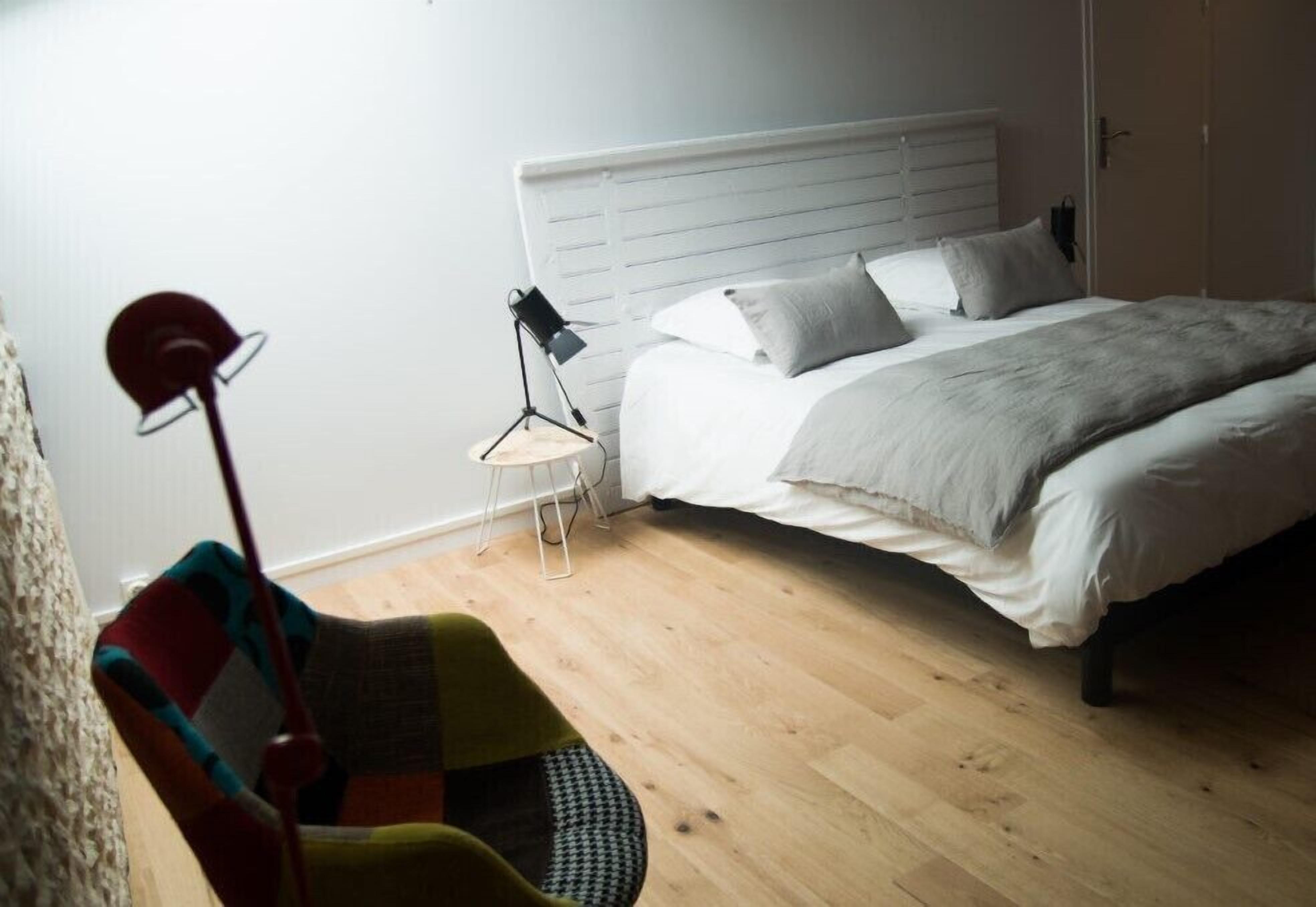 Un dormitorio con cama, una silla, una lámpara y un radiador.