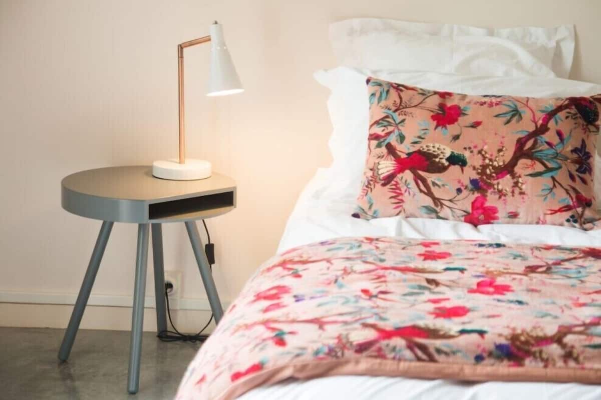 Ein Bett mit floralem Überwurf und ein Nachttisch mit Lampe.