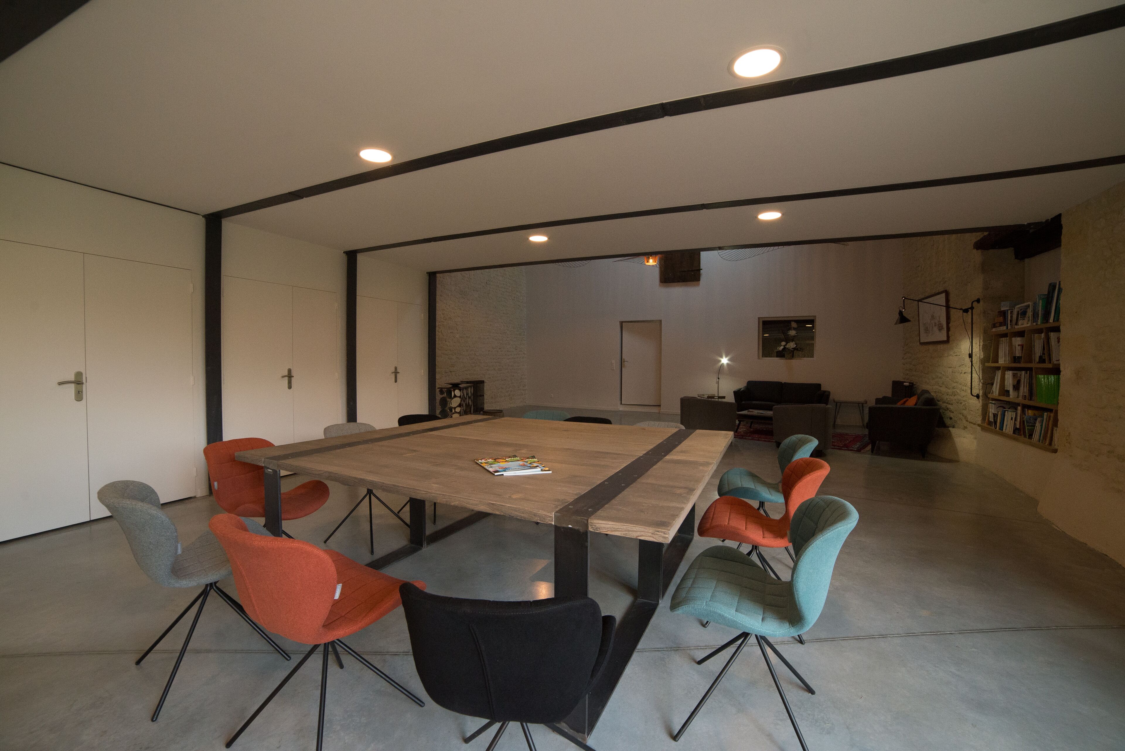 Uma sala de reunião moderna com uma grande mesa retangular, seis cadeiras e uma estante de livros ao fundo.