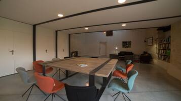 Uma sala de reunião moderna com uma grande mesa retangular, seis cadeiras e uma estante de livros ao fundo.