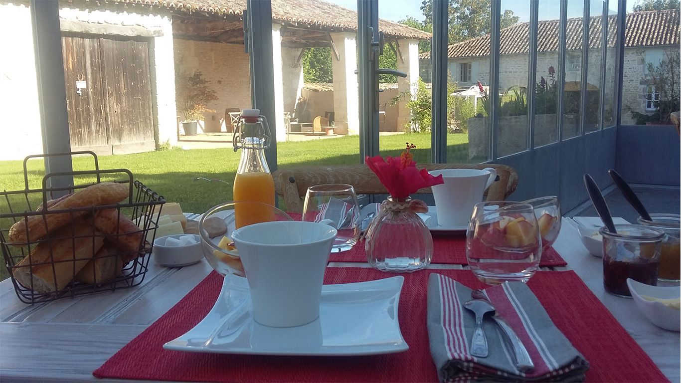 A breakfast table set with white plates, a basket of bread, a glass of orange juice, and a pitcher of water.