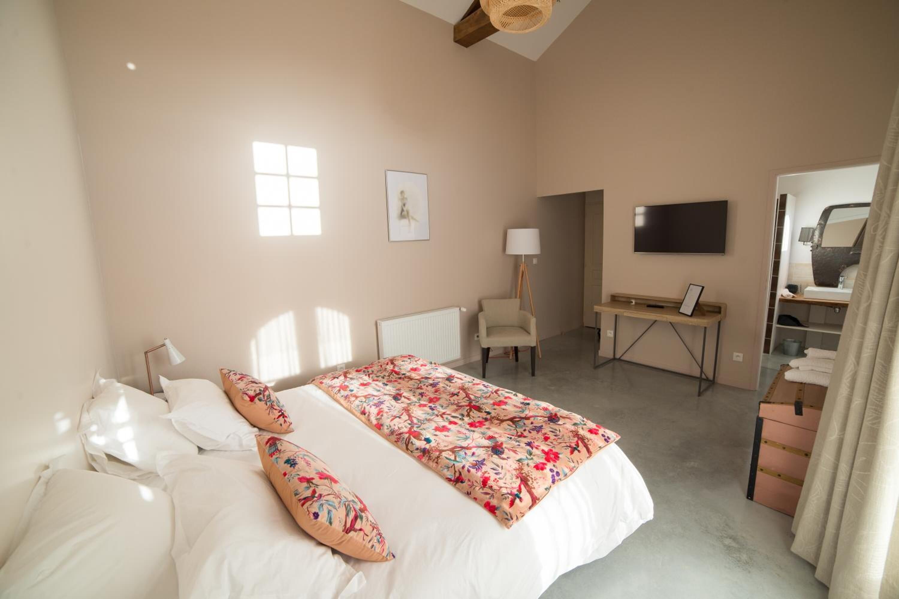 A bedroom with a bed, a desk, a chair, a TV, and a window.