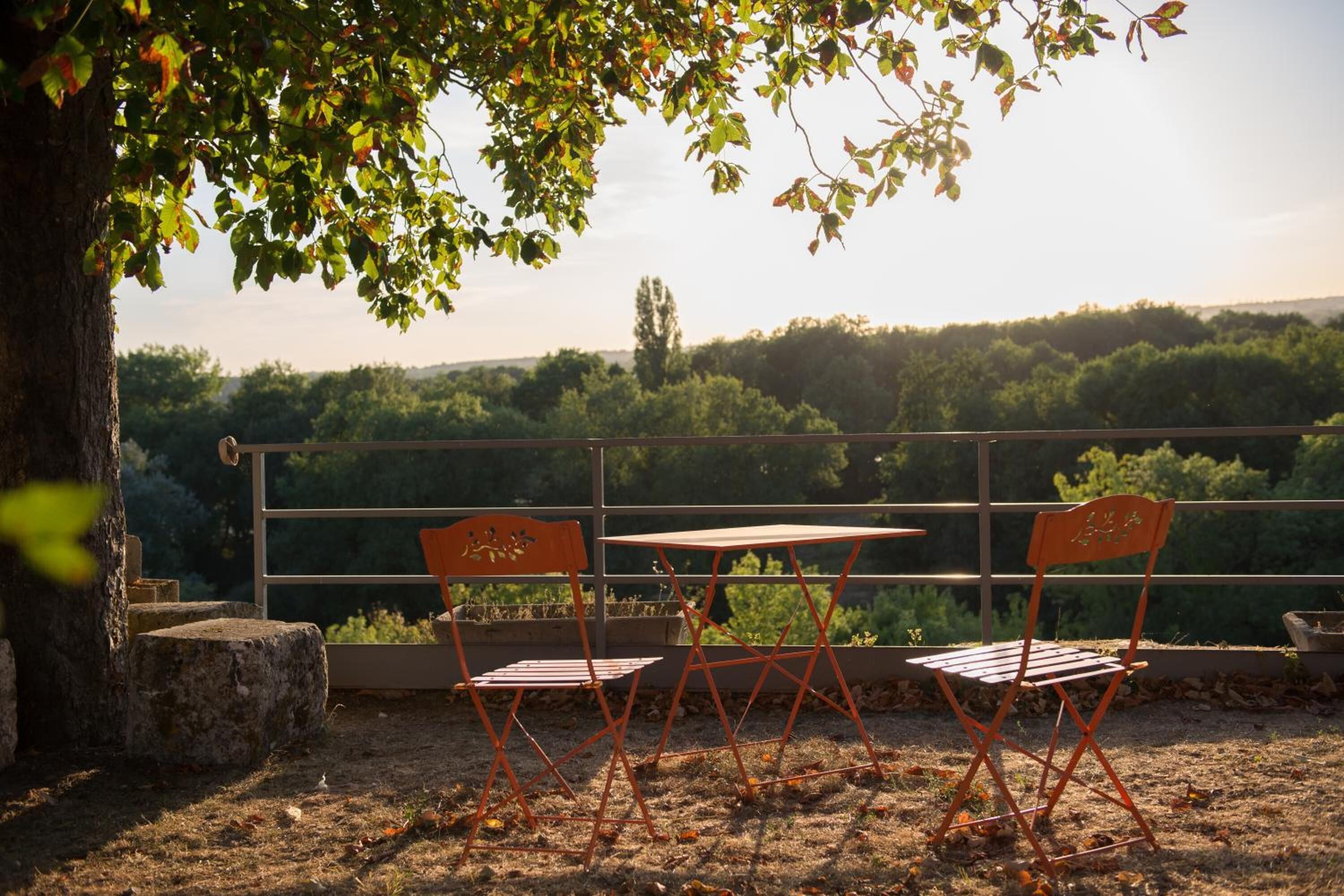 A terrace with a table and two chairs, overlooking a forested landscape.