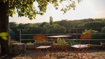 A terrace with a table and two chairs, overlooking a forested landscape.