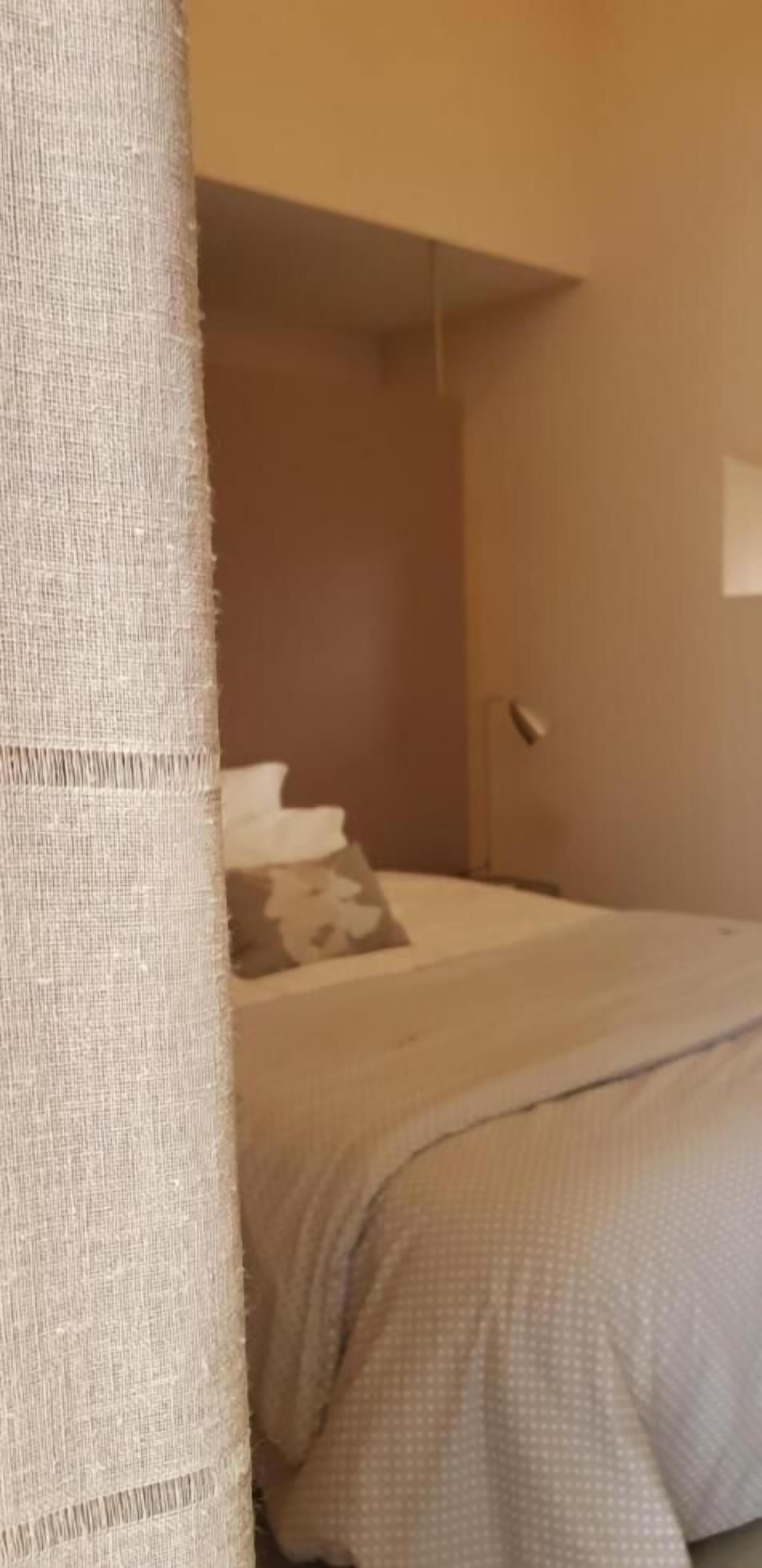 A bedroom with a bed, a nightstand, and a wall-mounted lamp.