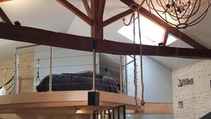 Un loft espacioso con vigas de madera a la vista, un entrepiso y una cocina moderna, además de una gran lámpara de araña.