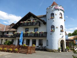 Um edifício com uma torre identificada com 'GASTHOF' e uma varanda com caixas de flores.