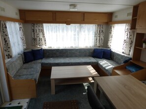 A compact RV interior with a sofa, a table, and a small kitchenette area.