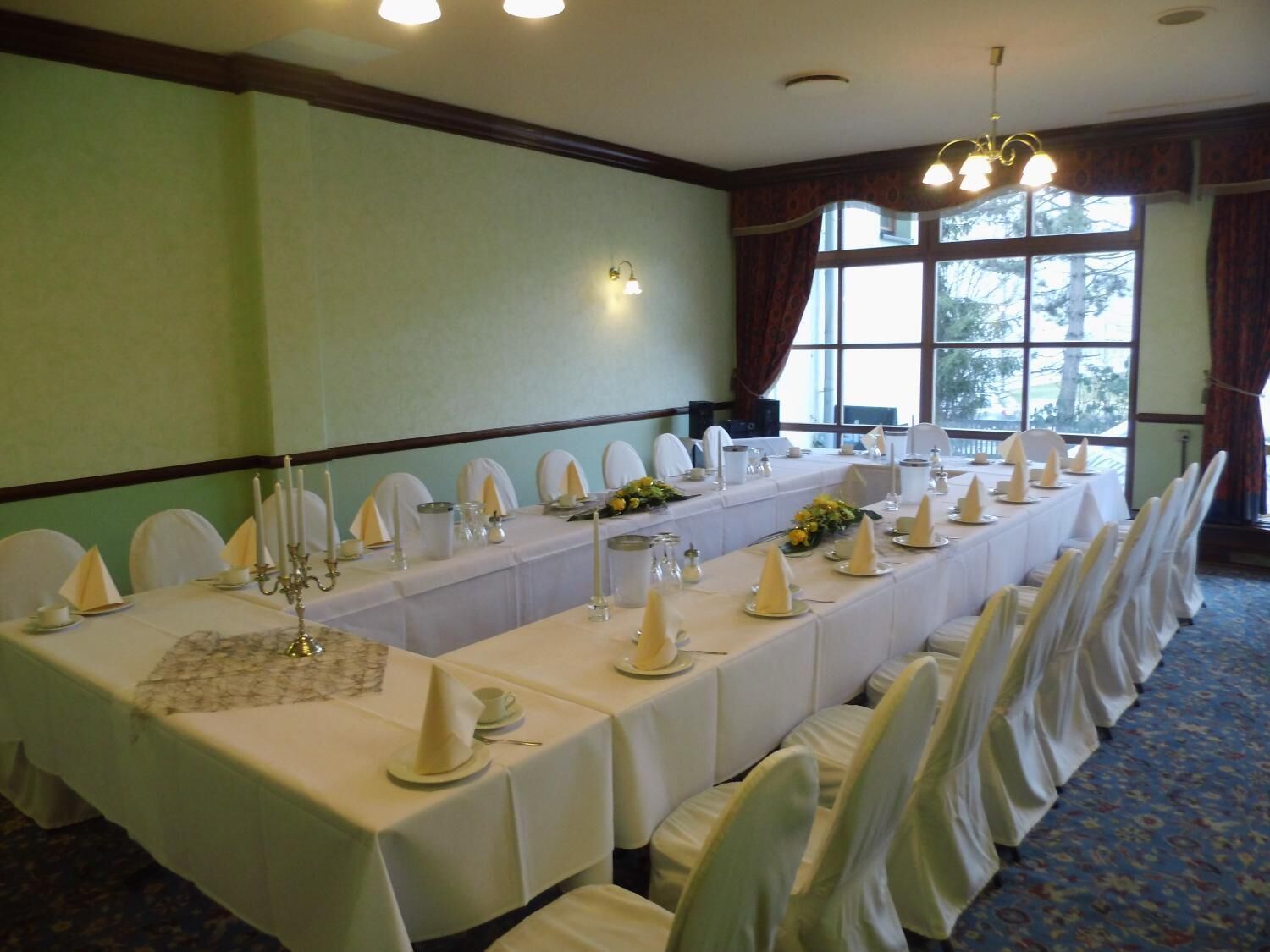 Un salón de conferencias con una larga mesa dispuesta para una reunión, sillas blancas y una araña.