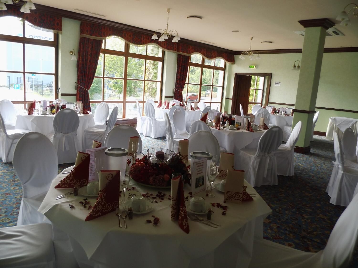 A banquet hall with round tables set for a formal event, featuring white tablecloths, chairs with white covers, and floral centerpieces.