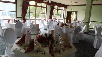 A banquet hall with round tables set for a formal event, featuring white tablecloths, chairs with white covers, and floral centerpieces.